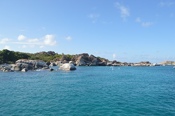 Sailing through crystal-clear waters with rocky coastline and lush greenery under a bright blue sky. Perfect island escape.
