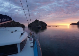 Sailing boat at sunset in a calm bay, surrounded by rocky islands and vibrant skies. Ideal for yacht charters.