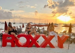 Beach sunset at 'Roxxy' with boats anchored in the distance, capturing vibrant seaside relaxation and summer vibes.