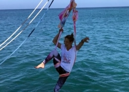 Aerial acrobatics on a sailboat with turquoise sea backdrop. Coastal adventure and sailing fun captured perfectly.