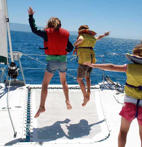 Kids bouncing on the catamaran trampoline on a family sailing vacation