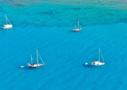 Sailing boats anchored on turquoise waters near a rocky coastline, perfect for a serene maritime escape.