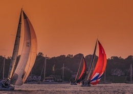 Sailboats with colorful spinnakers on a tranquil sea at sunset, creating a picturesque scene for sailing enthusiasts.