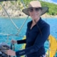 Woman enjoying a sunny day sailing with scenic coastal view in the background.