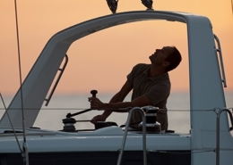 Sailor adjusting sail on a yacht at sunset, mastering navigation for a smooth maritime journey.