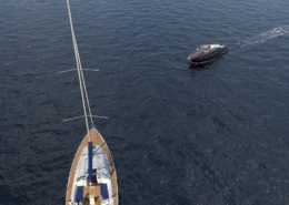 Sailboat and motorboat on calm sea, aerial view. Peaceful ocean cruising scene.