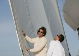 Two people enjoying a sunny day sailing, adjusting sails on a boat with clear blue skies in the background.