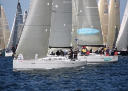 Sailboats racing in the ocean with crews managing sails, showcasing competitive sailing dynamics and teamwork.