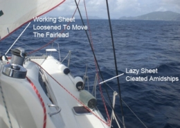 Sailing yacht adjusting sheets: working sheet loosened to move fairlead, lazy sheet cleated amidships over scenic ocean.