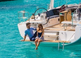 Couple relaxing on sailboat deck, enjoying sunny day on turquoise waters. Dream yachting escape in paradise.