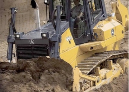 Bulldozer moving sand at a construction site, operated by a person in the driver's seat, surrounded by earthy terrain.