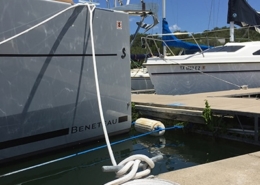 Sailboat docked at a marina with a neatly coiled rope on the pier under a clear blue sky.