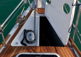 Open yacht anchor locker with chain and windlass, showcasing teak deck and railing against blue sea backdrop.