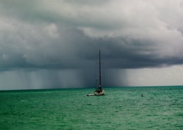 Sailboat on emerald sea approaches stormy skies, showcasing adventure and the thrill of sailing challenges.