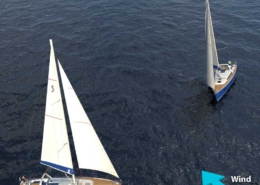 Two sailboats navigating in open sea, one with red hull. Wind direction indicated by blue arrow.