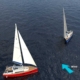 Two sailboats navigating in open sea, one with red hull. Wind direction indicated by blue arrow.