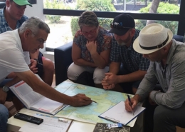 Group of people planning a sailing route with a map and notes in a cozy room, discussing navigation strategies.