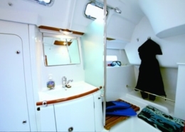 Sailboat interior bathroom with mirror, sink, and hangers for gear, showcasing efficient use of small space.