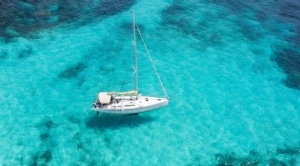 Sailboat anchored on crystal-clear turquoise sea, top view of idyllic sailing adventure destination.