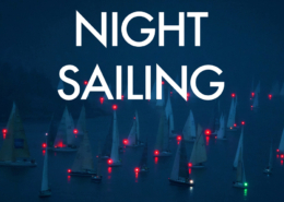 Sailboats with red lights navigate the water during a serene night sailing event.