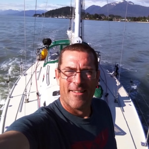 Man enjoying a solo sailing adventure on a scenic lake with mountainous backdrop.