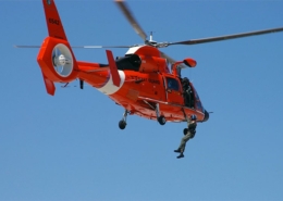 Coast Guard rescue helicopter with a crew member performing a daring sea operation in clear blue skies.