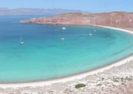 Panoramic view of a serene bay with turquoise waters, anchored sailboats, and a sandy beach, perfect for a sailing adventure.