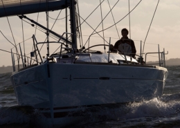 Sailing yacht gliding through ocean waves at sunset, sailor steering from deck, capturing adventure and freedom at sea.