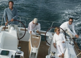 Group enjoying a sailing trip on a yacht, navigating through open sea with two steering wheels and wooden deck.