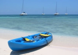 Blue kayak on a sandy beach with sailboats in the calm sea under a clear sky. Perfect day for sailing and kayaking.