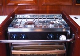 Sleek yacht interior featuring a shiny stainless steel stove and oven set within polished wooden cabinetry.