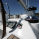 Close-up of a sailboat cockpit with winch, steering wheel, and navigation instruments under a clear blue sky.