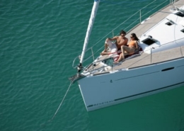 Couple relaxing on the deck of a sailing yacht, enjoying a sunny day on clear blue water.