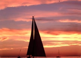 Sailboat gliding on calm sea during a vibrant sunset, highlighting the beauty of sailing at dusk.