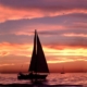 Sailboat gliding on calm sea during a vibrant sunset, highlighting the beauty of sailing at dusk.