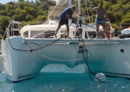 Sailing enthusiasts securing anchor on catamaran in serene blue waters, surrounded by lush green scenery.