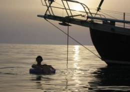 Person relaxing on an inflatable chair near a sailboat at sunset, serene ocean views, perfect for a peaceful sailing adventure.