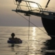 Person relaxing on an inflatable chair near a sailboat at sunset, serene ocean views, perfect for a peaceful sailing adventure.