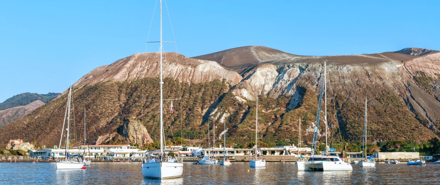 Sailboats anchored in calm waters near a stunning coastal landscape under a clear blue sky.