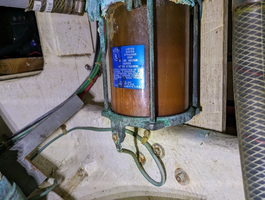 Close-up of a marine water strainer in a sailboat engine compartment, showcasing essential maintenance equipment.