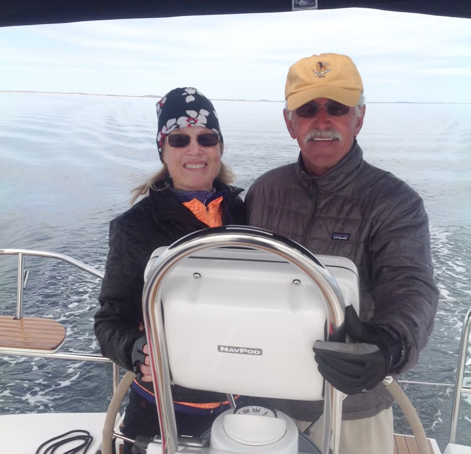 Captain Waddell sailing on a calm sea, smiling at the helm of their boat under a clear sky.