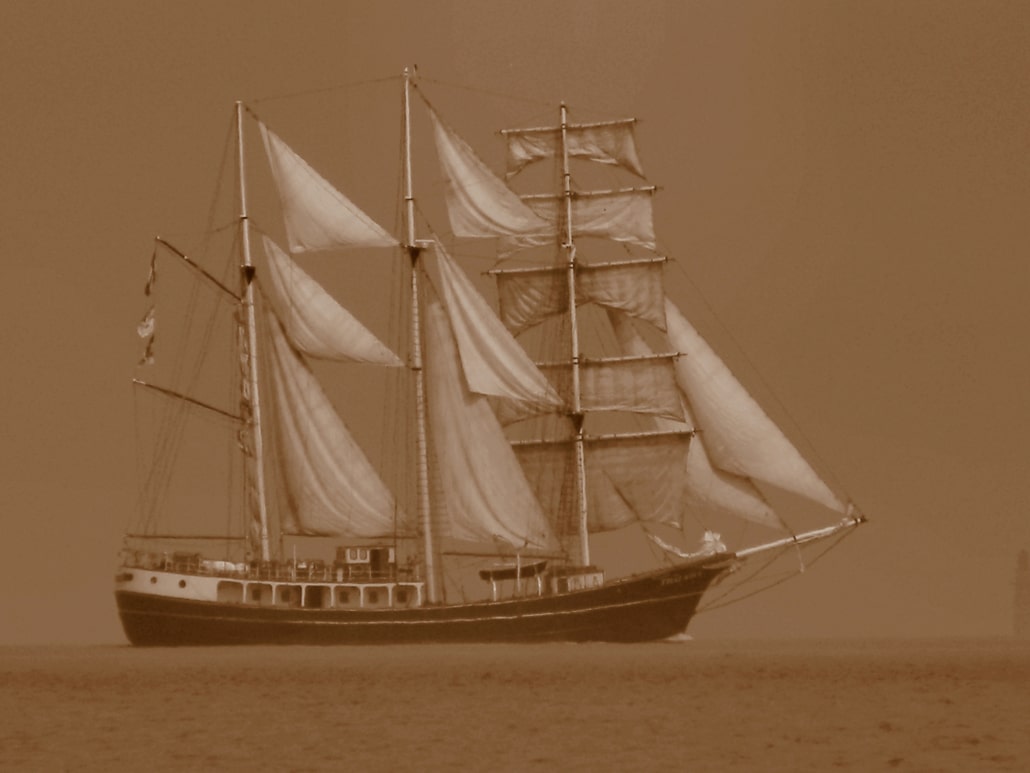 Sepia-toned image of a majestic sailing ship with billowing sails on a calm sea.