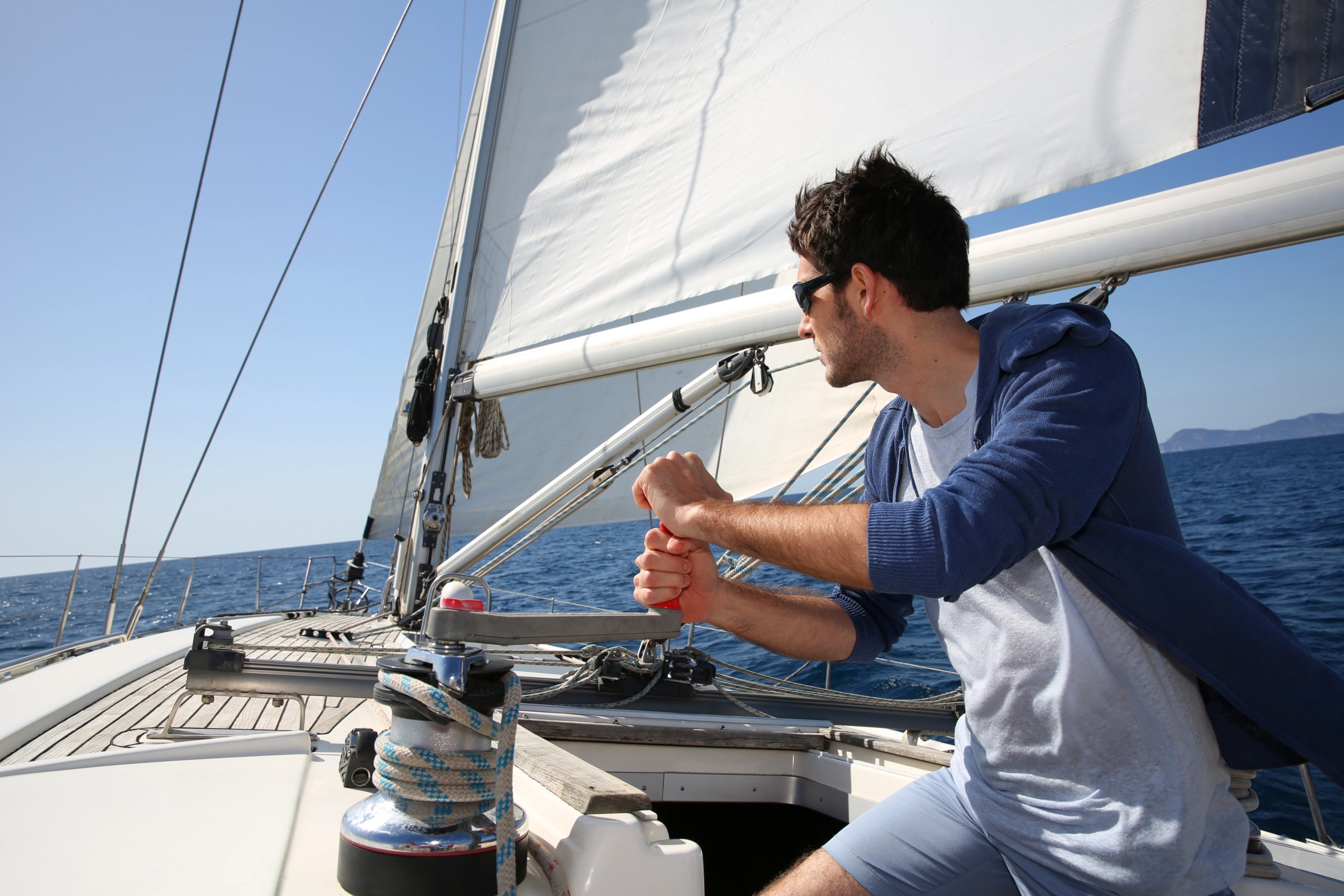 Man steering sailboat on open sea, enjoying sunny day and adventure sailing experience.