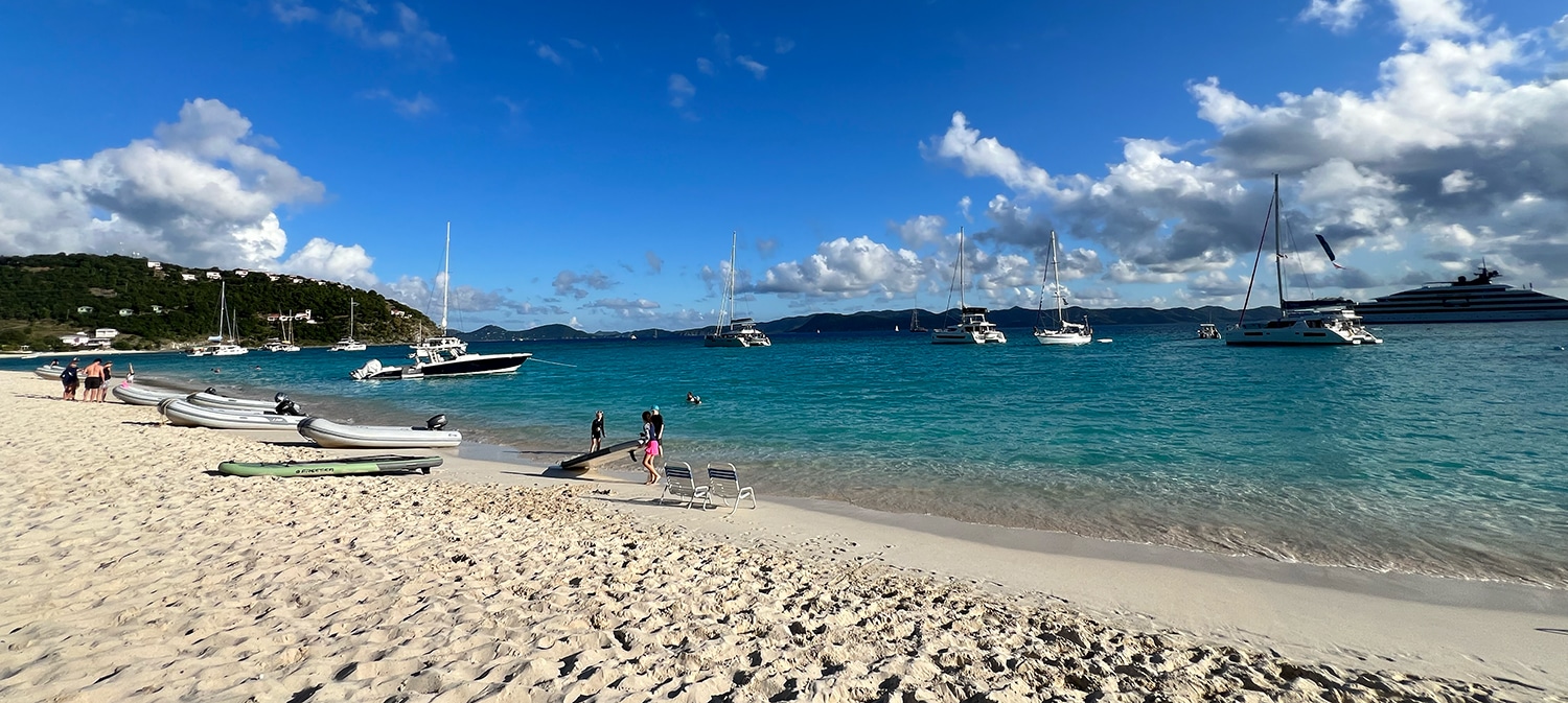 Sandy beach with boats anchored in turquoise ocean, under clear blue sky. Perfect sailing weather.