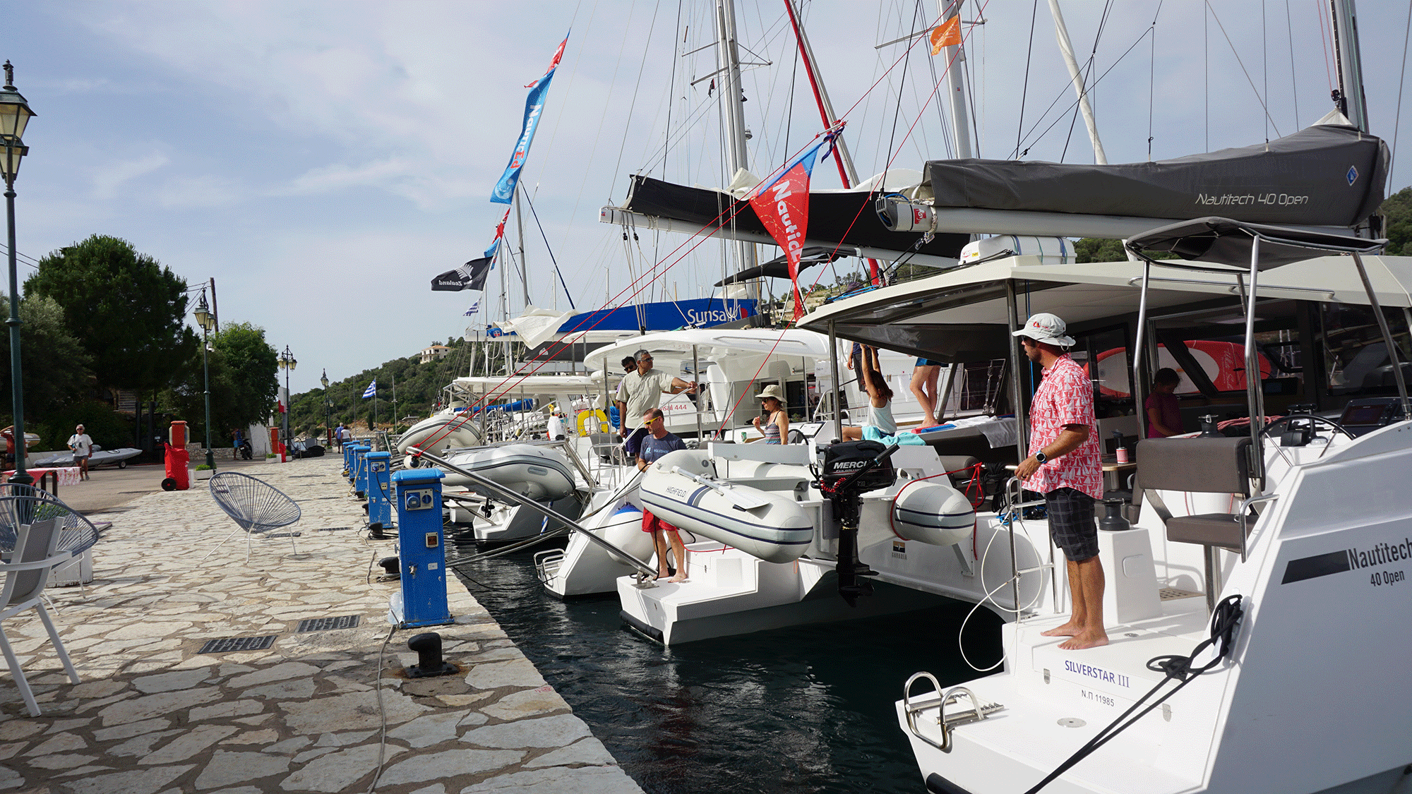 Sailboats docked at a marina with people preparing for a sailing adventure on a sunny day.