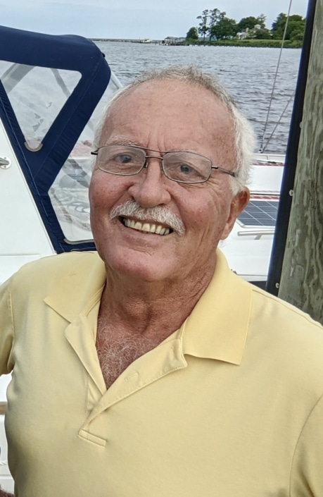 Smiling man on a sailboat by the water, wearing a yellow polo shirt, enjoying a day of sailing.