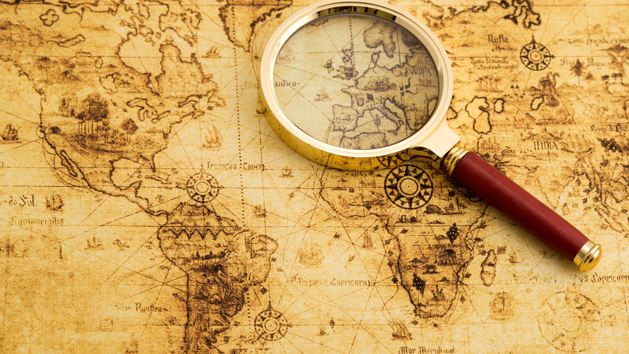 Vintage world map with a magnifying glass highlighting Europe and Africa, evoking exploration and adventure.