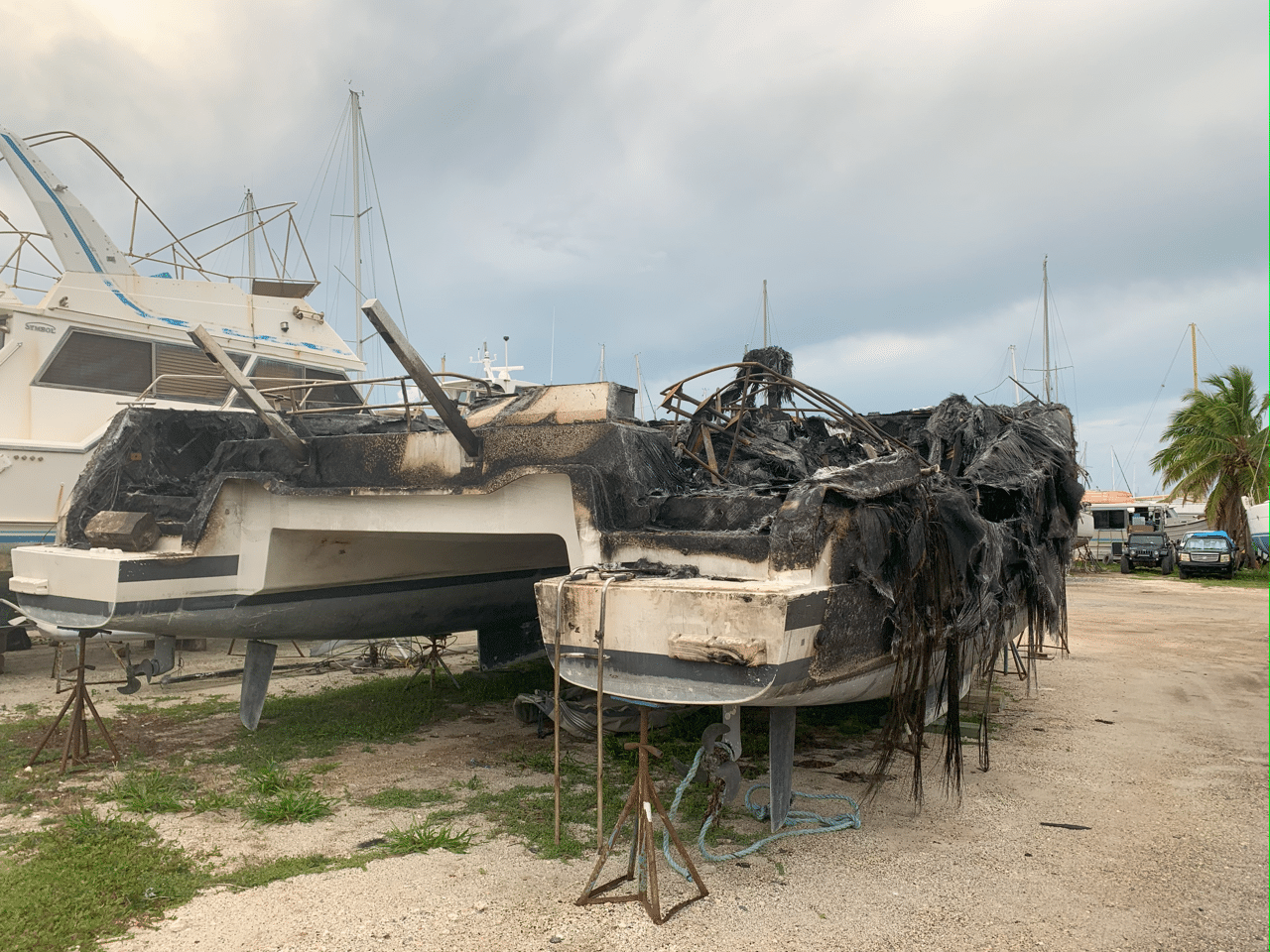 A fire-damaged shore power cord with visible burn marks and melted insulation, lying on the dock near a boat in Key West. Evidence of an electrical fire suggests the cord as the likely source of the incident.