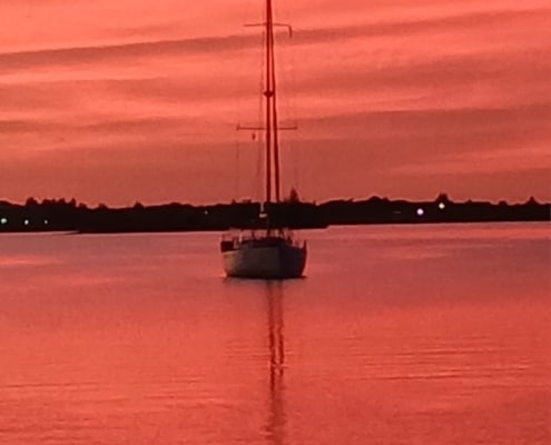 Sailboat on calm water at sunset with vibrant pink and orange sky, reflecting peaceful maritime scenery.