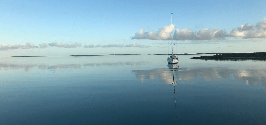 Sailboat on calm, reflective waters under a clear sky, perfect serene sailing scene.